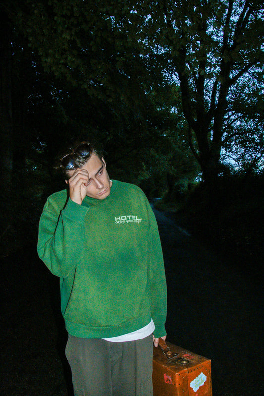 Person in a green sweatshirt with 'HOTEL' text, holding a phone to their ear outdoors at night.